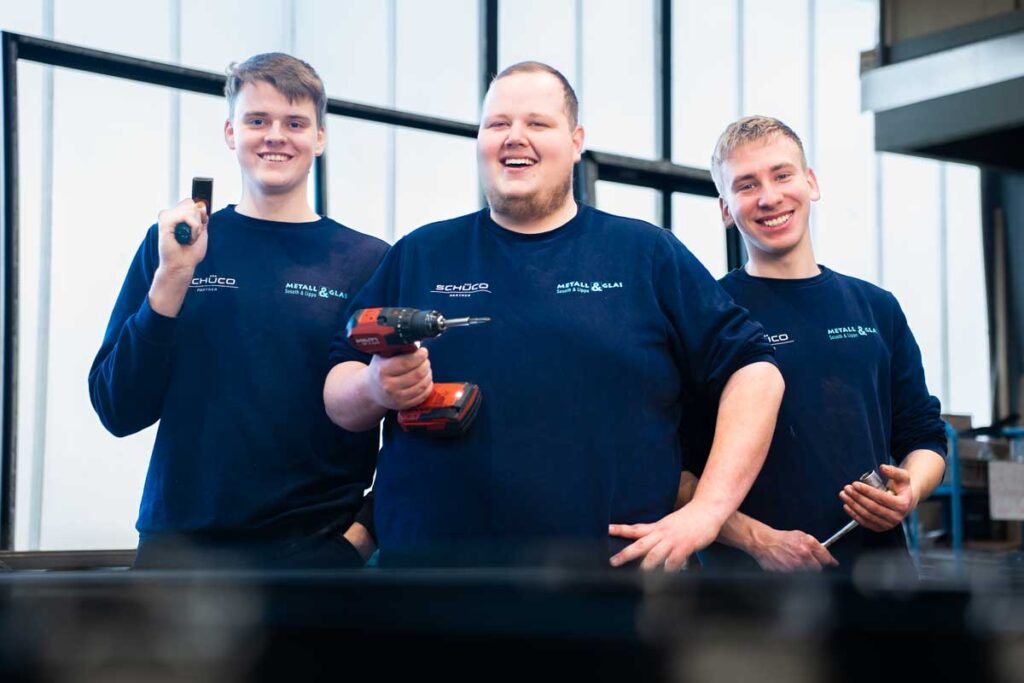 Drei Azubis in der Werkstatt lächeln in die Kamera