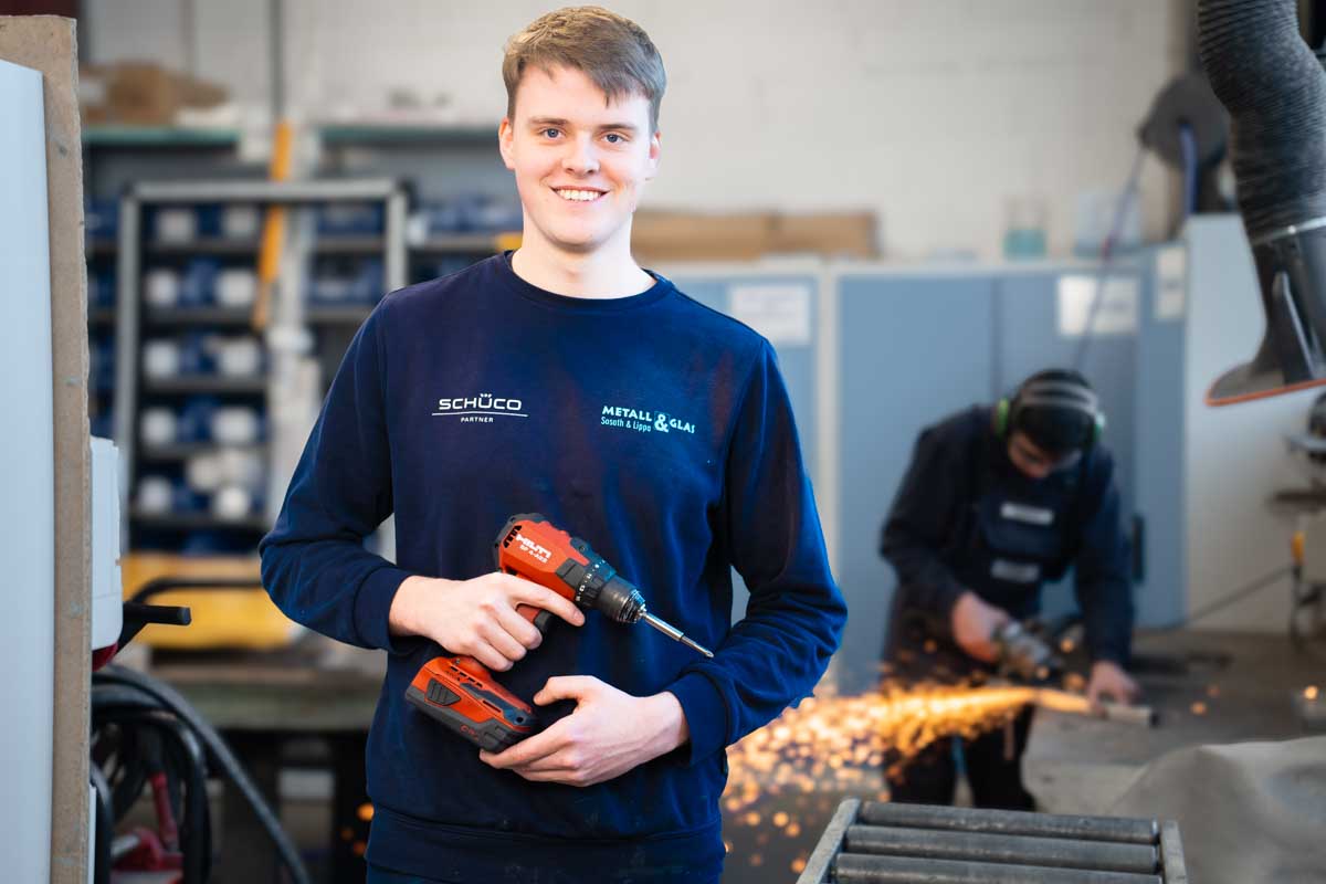 Azubi mit einer Bohrmaschine in der Hand schaut in die Kamera