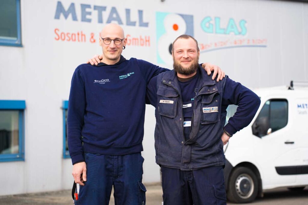 Zwei Mitarbeiter vor einer Werkshalle mit Armen auf den Schultern