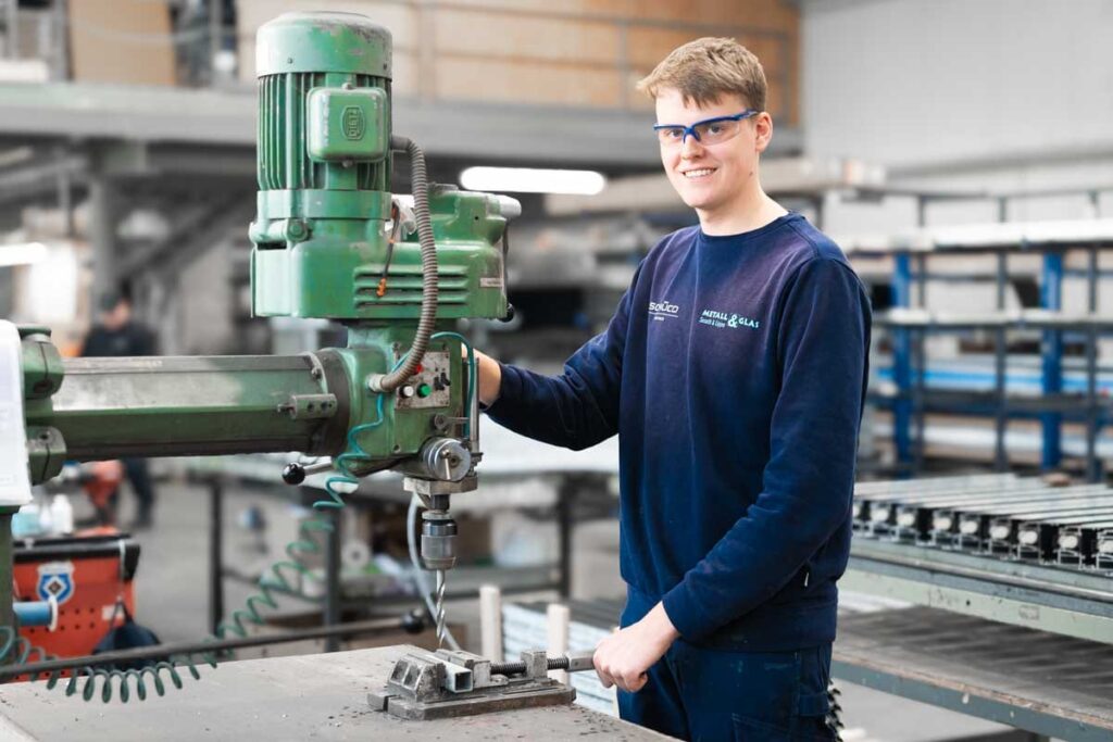 Azubi an einer Standbohrmaschine schaut in die Kamera