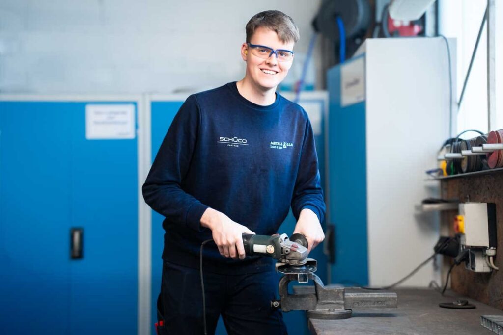 Azubi mit einem Winkelschleifer in der Hand schaut in die Kamera